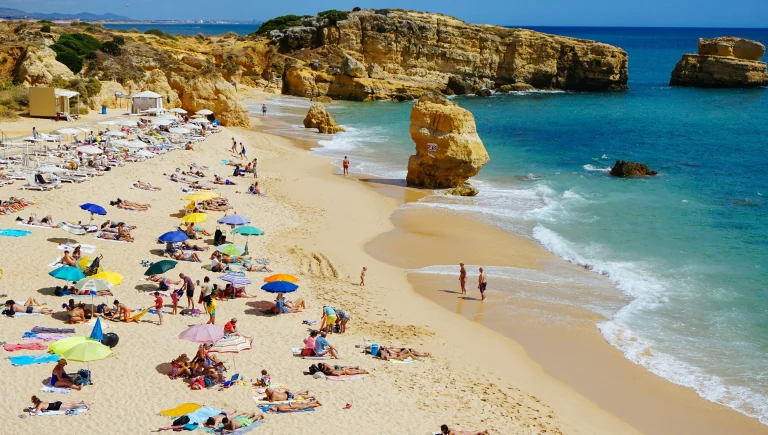 Plage de sable doré bordée de falaises rocheuses et d’eaux turquoise sur la côte de l’Algarve au Portugal.