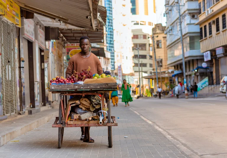 Vendeur ambulant poussant une charrette chargée de fruits frais dans une rue commerçante animée d'Afrique de l'Est.