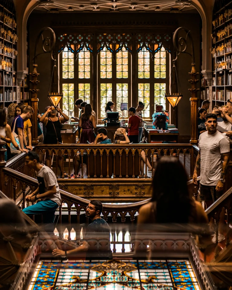 Intérieur d’une librairie historique aux boiseries sculptées, vitraux colorés et escaliers fréquentés par les visiteurs