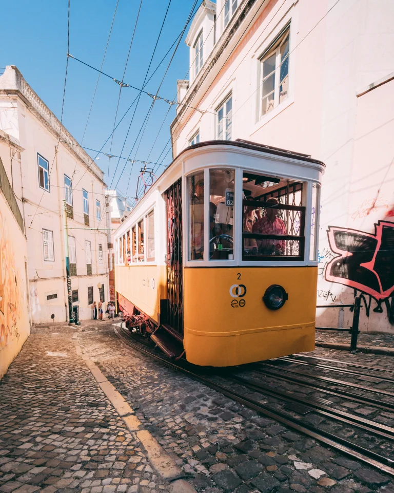 Tramway jaune traditionnel circulant dans une rue pavée et pentue de Lisbonne, entre les façades des immeubles.